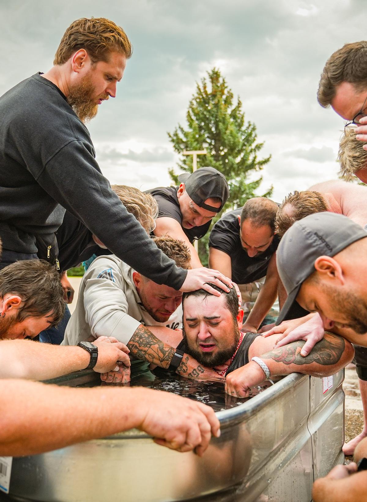 Men laying hands on a brother in the ice bath and praying over him